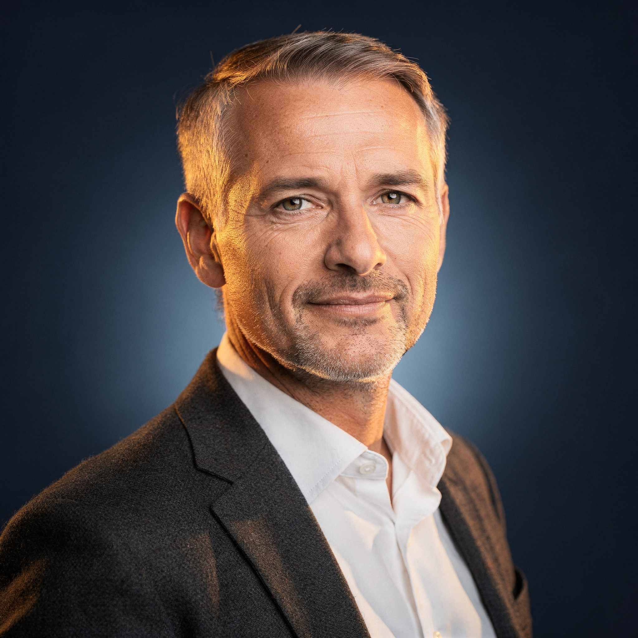 Calm grey-haired man in a charcoal blazer looking at the camera